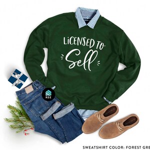May include: A forest green sweatshirt with the text "Licensed to Sell" in white lettering. The sweatshirt is paired with blue jeans, a plaid shirt, and brown leather shoes.