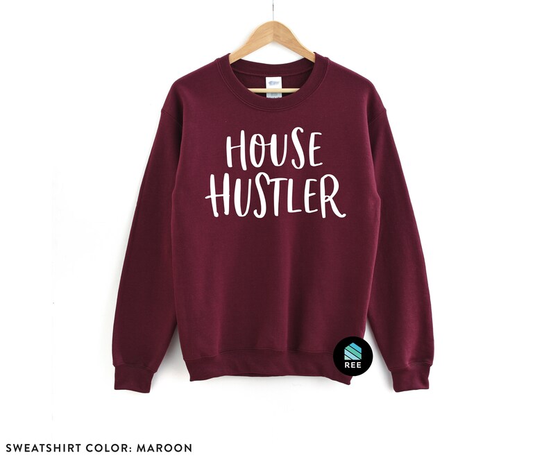 Peut inclure: Sweat-shirt bordeaux avec l'inscription blanche &laquo; HOUSE HUSTLER &raquo;. Le sweat-shirt est suspendu &agrave; un cintre en bois sur fond blanc. Col rond, couleur unie.