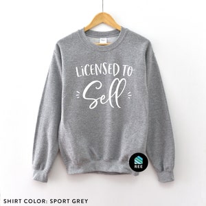 May include: A gray sweatshirt with the text "Licensed to Sell" in white lettering. The sweatshirt is hanging on a wooden hanger.