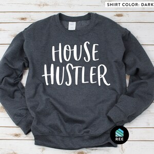 Peut inclure: Sweat-shirt gris fonc&eacute; avec le texte blanc "HOUSE HUSTLER". Ce sweat-shirt &agrave; col rond a des manches longues. La couleur du t-shirt est gris fonc&eacute;.