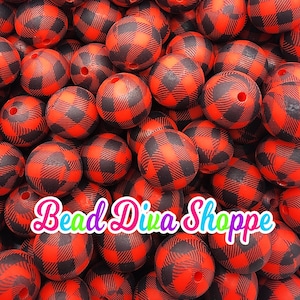 May include: A collection of red and black plaid beads. The beads are round with a hole through the center. The text "Bead Diva Shoppe" is displayed across the bottom of the image in a colorful font. These beads are suitable for jewelry making.