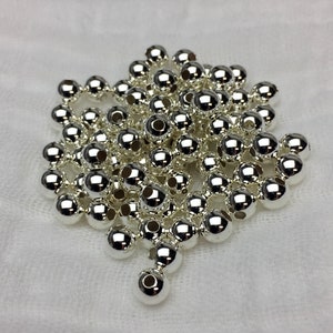 Puede incluir: Un mont&oacute;n de cuentas de metal de color plateado. Las cuentas son redondas y tienen un acabado liso y brillante.
