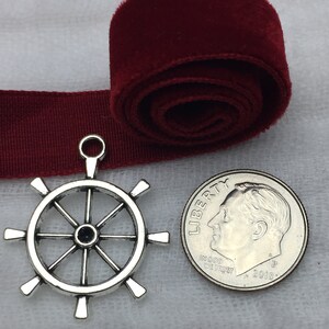 May include: Silver-toned metal ship wheel charm pendant with eight spokes. The charm is about the size of a US dime.