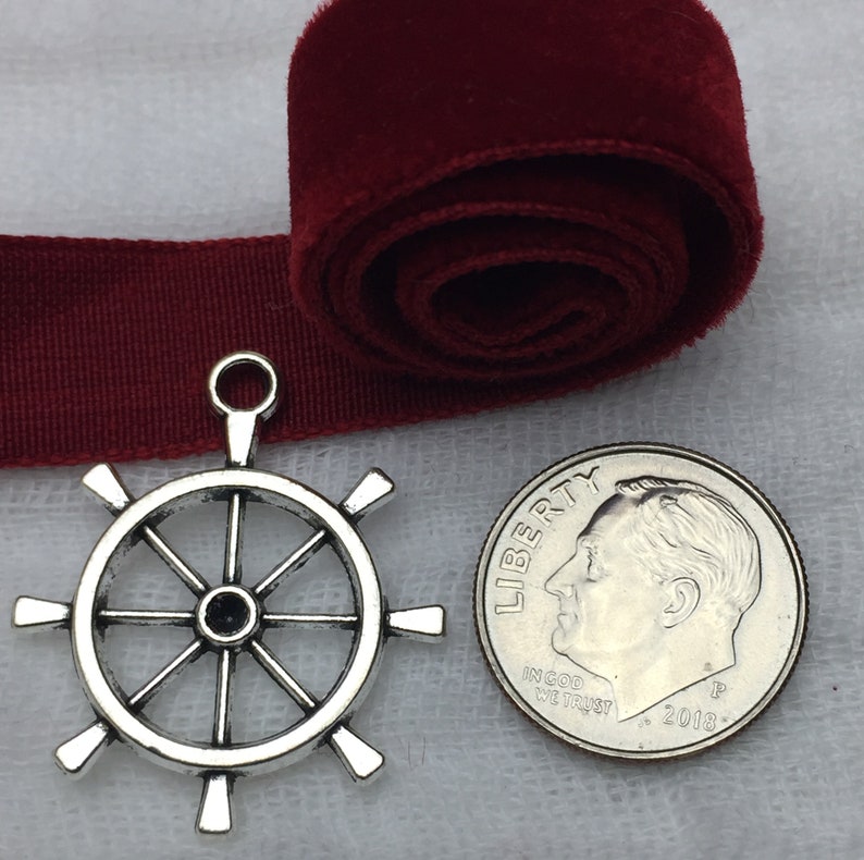 May include: Silver-toned metal ship wheel charm pendant with eight spokes. The charm is about the size of a US dime.