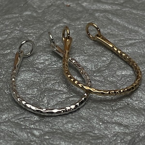 May include: Close-up of two teardrop-shaped earrings. One earring is silver-colored, and the other is gold-colored. Both earrings have a hammered texture and a small loop at the top for hanging.