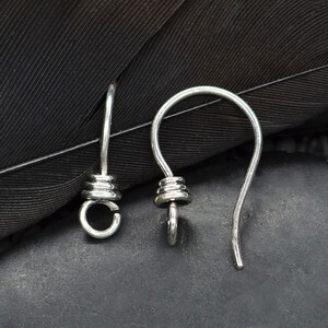 May include: Two silver-toned earring hooks featuring a curved wire design and a small, coiled decorative element at the base. Each hook includes a circular loop at the bottom for attaching jewelry components, with a smooth, polished metallic finish.