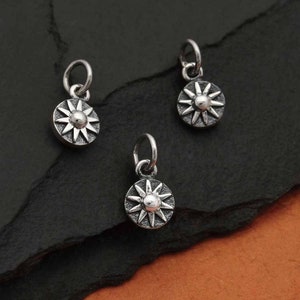 May include: Three silver charm pendants in the shape of a sun with a raised centre. The charms are on a dark grey background.