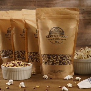Puede incluir: Cuatro bolsas de papel marrón llenas de granos de maíz para palomitas de maíz. Las bolsas están etiquetadas con "Seven Forks Farm Family Grown Popcorn". La bolsa de la parte delantera está etiquetada con "Autumn Medley Net Wt. 30oz."