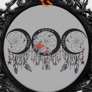 Puede incluir: Un patrón de punto de cruz en blanco y negro de tres lunas crecientes con atrapasueños y plumas que cuelgan de ellas. Las lunas están rodeadas de pequeñas bayas rojas y flores blancas. El patrón está enmarcado en un marco negro adornado.