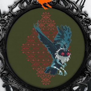 Puede incluir: Un patrón de punto de cruz de una criatura azul y verde con ojos rojos, volando sobre un fondo rojo y verde. La criatura está rodeada de un patrón geométrico rojo y verde. El patrón está enmarcado en un marco negro adornado.