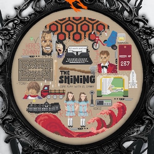 Puede incluir: Un punto de cruz enmarcado con escenas de la película "El Resplandor". La obra de arte incluye imágenes icónicas como el laberinto, las gemelas y la frase "Here's Johnny". El marco negro tiene un diseño decorativo y está rodeado de ramas negras.