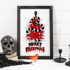 May include: A framed print of a red and black Christmas tree with the text "Merry Creepmas" in dripping red letters. The tree is decorated with skulls, bats, and a coffin. The print is on a white background and has a black frame.