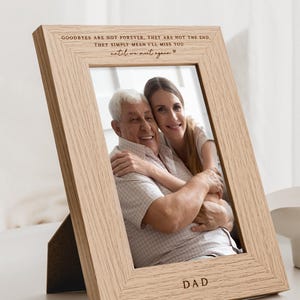 May include: A wooden photo frame with a light brown finish. The frame has a photo of an older man and a younger woman smiling. The frame has the text "GOODBYES ARE NOT FOREVER, THEY ARE NOT THE END. THEY SIMPLY MEAN I'LL MISS YOU UNTIL WE MEET AGAIN." and "DAD" engraved on it.