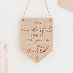 May include: Wooden sign with a white background and the text "How wonderful life is now you're in the world" in a cursive font.
