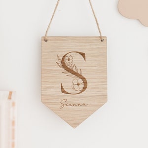 May include: Wooden banner with a floral design and the letter "S" in the centre. The name "Sienna" is written below the letter.