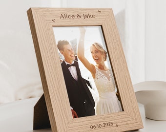 May include: A light wood photo frame with a personalized inscription that reads "Alice & Jake" and "06.10.2025". The frame features a photo of a couple smiling and holding hands.