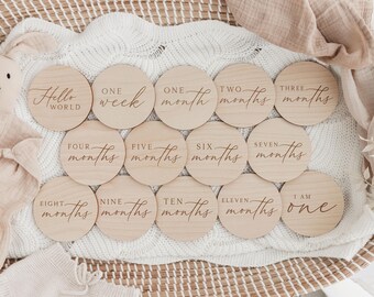 Puede incluir: Un conjunto de 12 discos de madera para hitos de bebé con un acabado de madera natural. Los discos presentan texto grabado, incluyendo "Hello World", "One Week", "One Month", "Two Months", "Three Months", "Four Months", "Five Months", "Six Months", "Seven Months", "Eight Months", "Nine Months", "Ten Months", "Eleven Months", y "I am One".