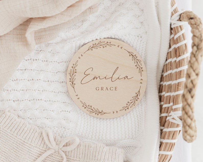 May include: A round wooden plaque with a floral design and the name "Emilia Grace" engraved in cursive.