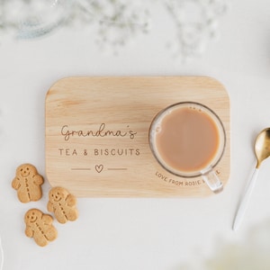 May include: A wooden serving tray with the words "Grandma's TEA & BISCUITS" and a heart symbol. A clear glass mug with tea, gingerbread cookies, and a gold and white spoon are on the tray. The words "Love from Rosie" are on the tray.