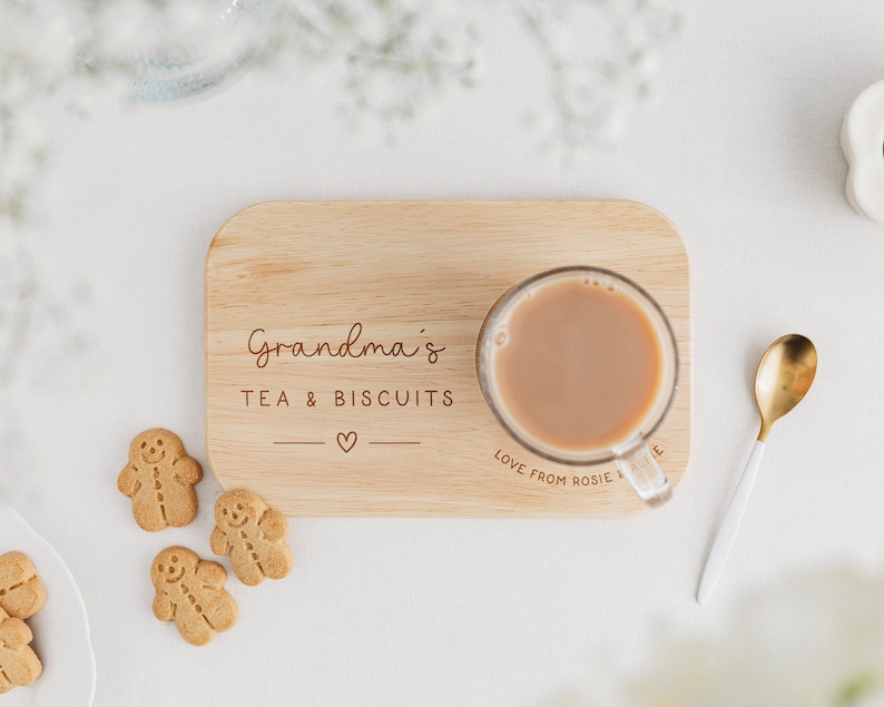 May include: A wooden serving tray with the words "Grandma's TEA & BISCUITS" and a heart symbol. A clear glass mug with tea, gingerbread cookies, and a gold and white spoon are on the tray. The words "Love from Rosie" are on the tray.