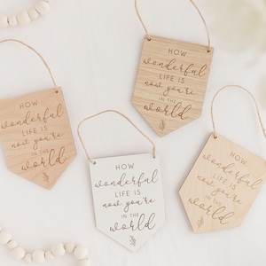 May include: Four wooden signs with the text "HOW wonderful LIFE IS now you're IN THE world" in a cursive font. The signs are in different colors, with two being natural wood and two being white.