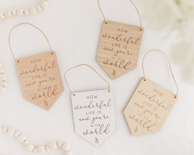 May include: Four wooden signs with the text "HOW wonderful LIFE IS now you're IN THE world" in a cursive font. The signs are in different colors, with two being natural wood and two being white.