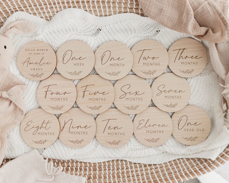 May include: A set of 12 wooden baby milestone discs with engraved text, including "Hello World, My Name Is Amelie Grace", "One Week", "One Month", "Two Months", "Three Months", "Four Months", "Five Months", "Six Months", "Seven Months", "Eight Months", "Nine Months", "Ten Months", "Eleven Months", and "One Year Old".