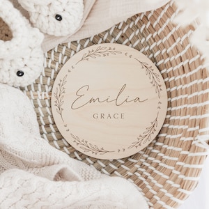 May include: A round wooden sign with a floral design and the name "Emilia Grace" engraved in a cursive font.