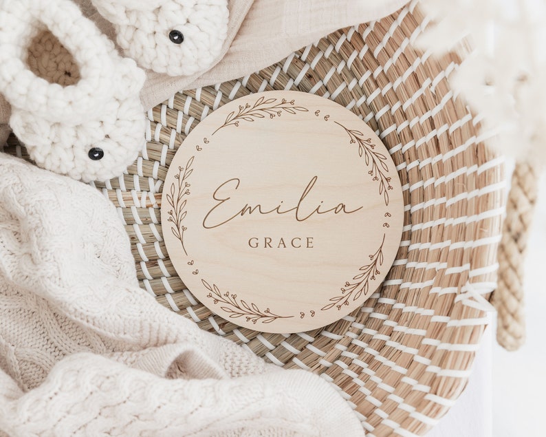 May include: A round wooden sign with a floral design and the name "Emilia Grace" engraved in a cursive font.