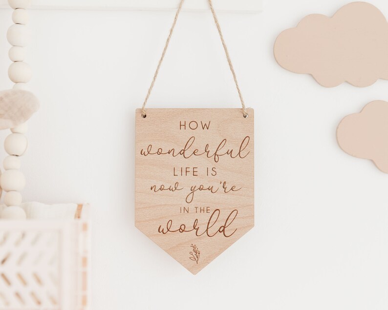 May include: Wooden sign with a white background and the text "How wonderful life is now you're in the world" in a cursive font.