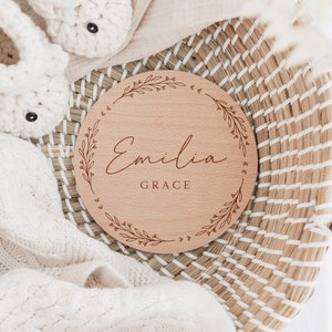 May include: A wooden round sign with a floral design and the name "Emilia Grace" engraved in cursive.