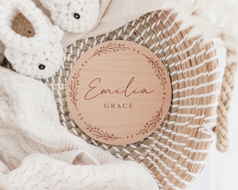 May include: A wooden round sign with a floral design and the name "Emilia Grace" engraved in cursive.