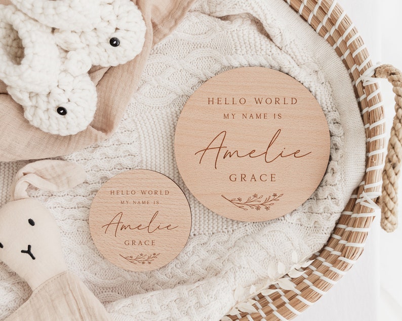 May include: Two wooden baby announcement plaques with the text "Hello World, My Name Is Amelie Grace" and a floral design.