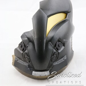 May include: A black and gold helmet with a yellow visor. The helmet has a textured surface and appears to be made of plastic. The helmet is a prop for cosplay or a movie.