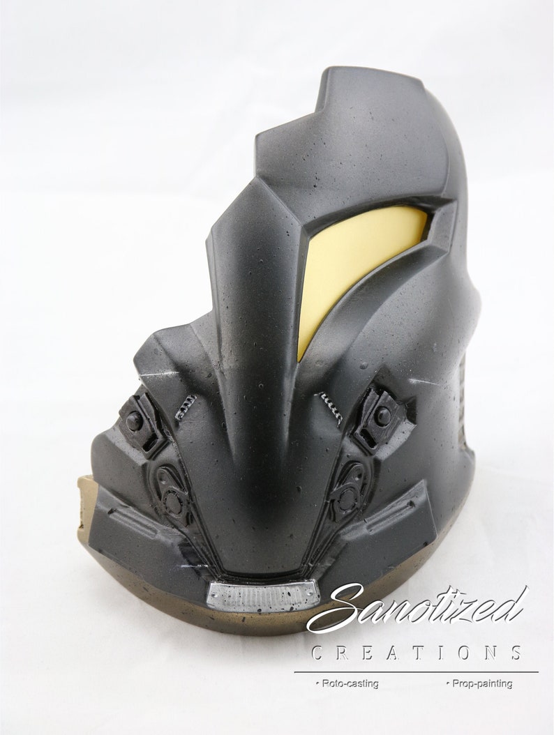 May include: A black and gold helmet with a yellow visor. The helmet has a textured surface and appears to be made of plastic. The helmet is a prop for cosplay or a movie.