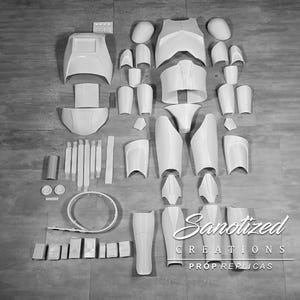 May include: A disassembled white prop armor set, including chest, shoulder, and leg pieces, arranged on a wooden surface. The set includes various components, such as arm guards and helmet pieces. The image also features the text "Sanotized Creations Prop Replicas."