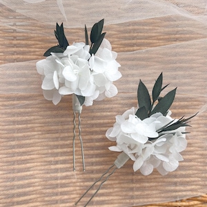 Puede incluir: Dos horquillas para el pelo con racimos de p&eacute;talos de hortensia blancos acentuados con hojas de color verde oscuro. Cada arreglo floral est&aacute; fijado a una horquilla de metal plateado en forma de U, dise&ntilde;ada para colocarla en el cabello.