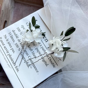 Puede incluir: Dos horquillas para el cabello con racimos de peque&ntilde;as flores de hortensia blancas y hojas de color verde oscuro. Cada horquilla tiene una base met&aacute;lica fina en forma de U, envuelta en cinta floral blanca para una sujeci&oacute;n segura y delicada.