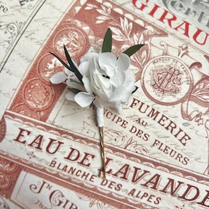 Puede incluir: Una horquilla para el pelo con un ramillete de p&eacute;talos de hortensia blancos y peque&ntilde;as hojas de color verde oscuro. El tallo del arreglo floral est&aacute; envuelto en cinta blanca y unido a una fina horquilla de metal dorado.