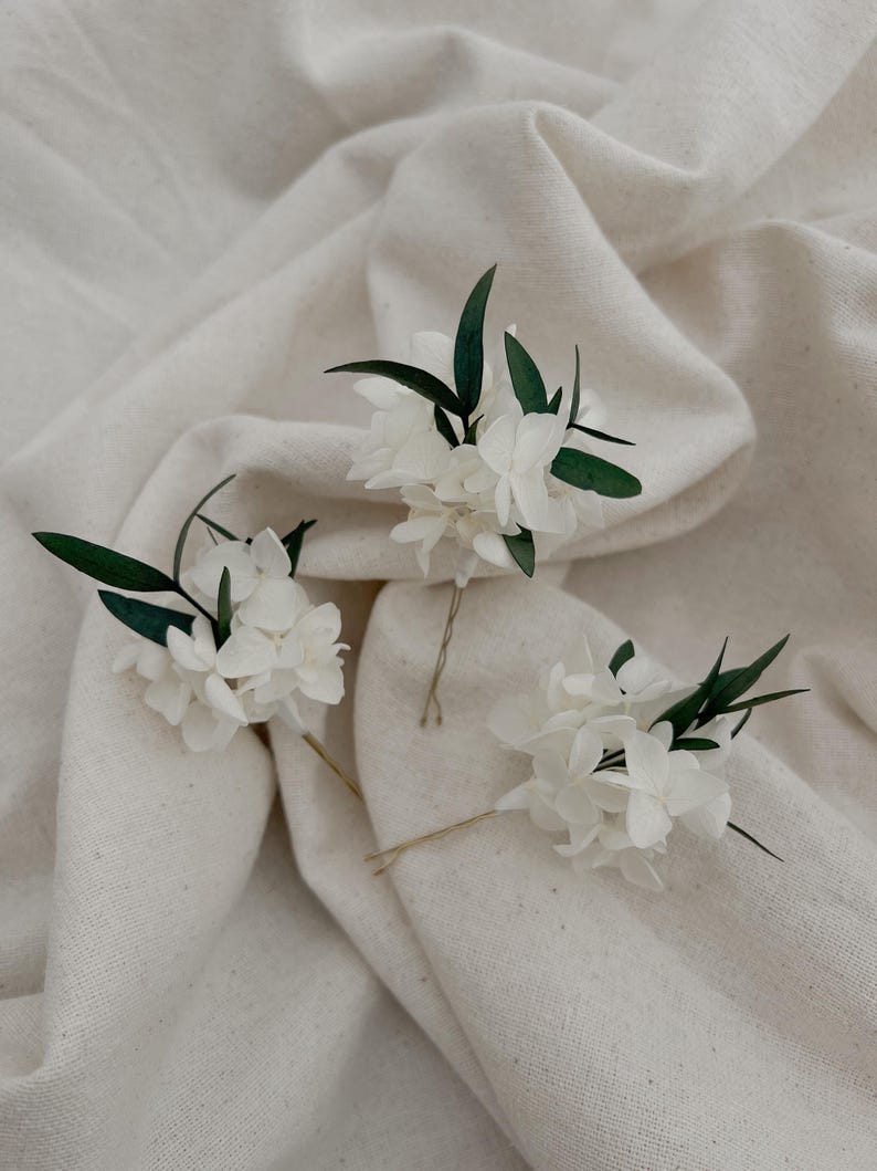 Puede incluir: Tres horquillas para el pelo con racimos de peque&ntilde;as flores blancas acentuadas con hojas finas de color verde oscuro. Cada arreglo floral est&aacute; unido a un alfiler de metal fino, dise&ntilde;ado para insertarse en el cabello como adorno floral.
