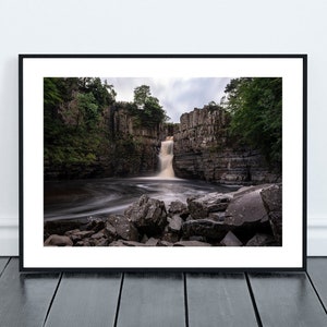 May include: A photograph of a waterfall cascading over a rocky cliff face. The water is flowing over the rocks and creating a mist. The surrounding area is covered in lush green trees.
