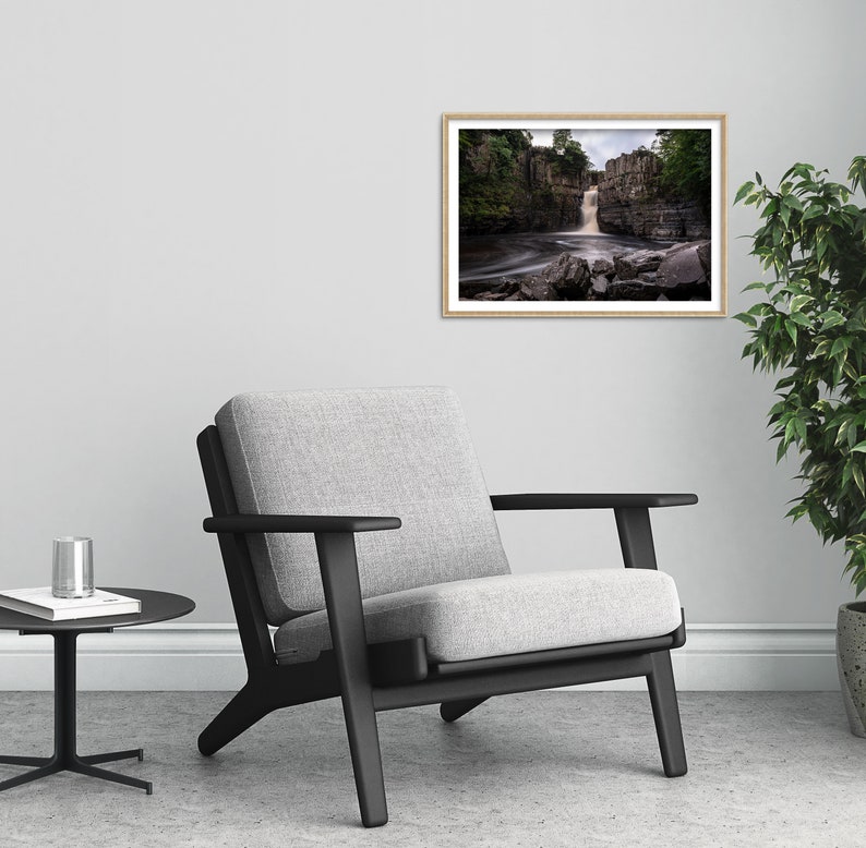 May include: A black armchair with a gray fabric seat and back, positioned in front of a white wall with a framed photograph of a waterfall in a forest setting.