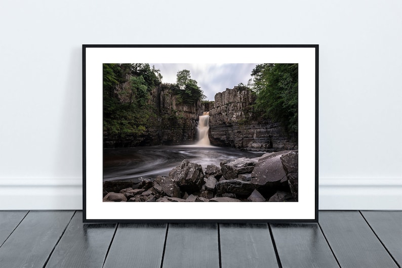 May include: A photograph of a waterfall cascading over a rocky cliff face. The water is flowing over the rocks and creating a mist. The surrounding area is covered in lush green trees.