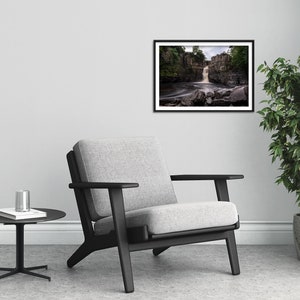 May include: A black and white framed photograph of a waterfall cascading over rocks in a lush green forest. The water is flowing over the rocks and creating a misty spray.