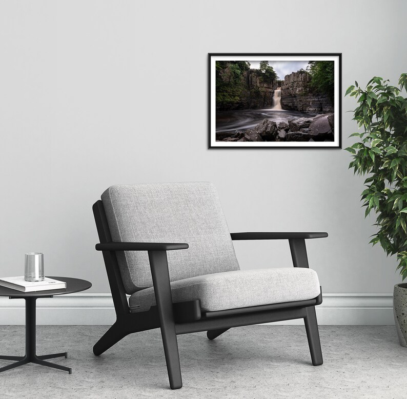 May include: A black and white framed photograph of a waterfall cascading over rocks in a lush green forest. The water is flowing over the rocks and creating a misty spray.