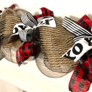 May include: A brown burlap and black and white striped ribbon Christmas wreath with the word "KOZY" written on it.