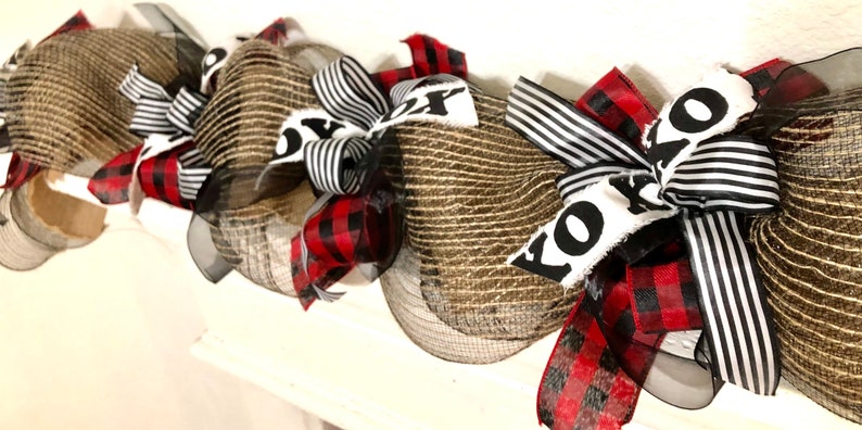May include: A brown burlap and black and white striped ribbon Christmas wreath with the word "KOZY" written on it.