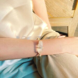 May include: A gold wire bracelet with a clear quartz crystal wrapped in the wire. The bracelet is on a person's wrist.
