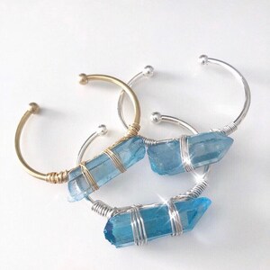 May include: Three wire-wrapped bracelets with blue crystal accents. The bracelets are made with silver and gold wire and feature a blue crystal wrapped in wire.