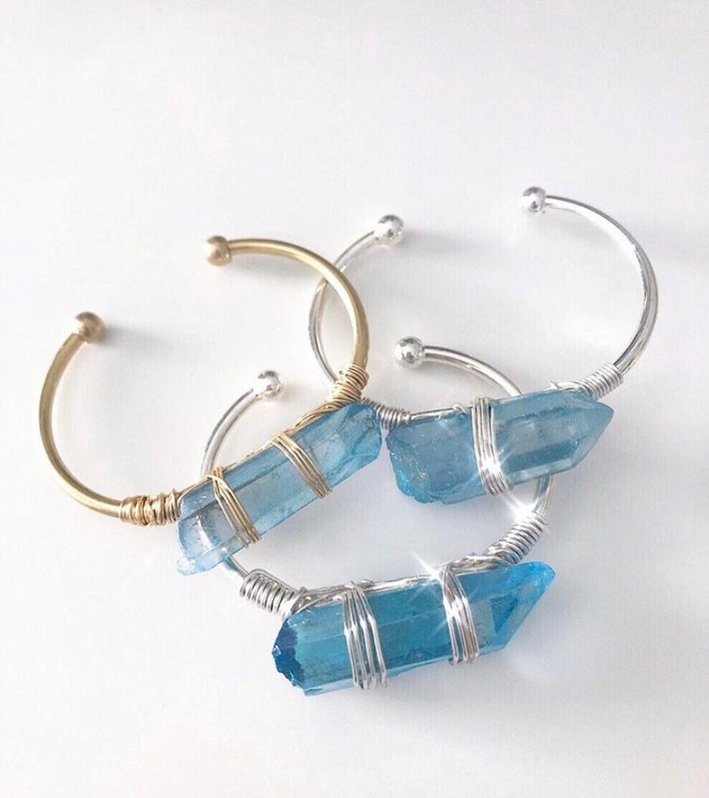 May include: Three wire-wrapped bracelets with blue crystal accents. The bracelets are made with silver and gold wire and feature a blue crystal wrapped in wire.